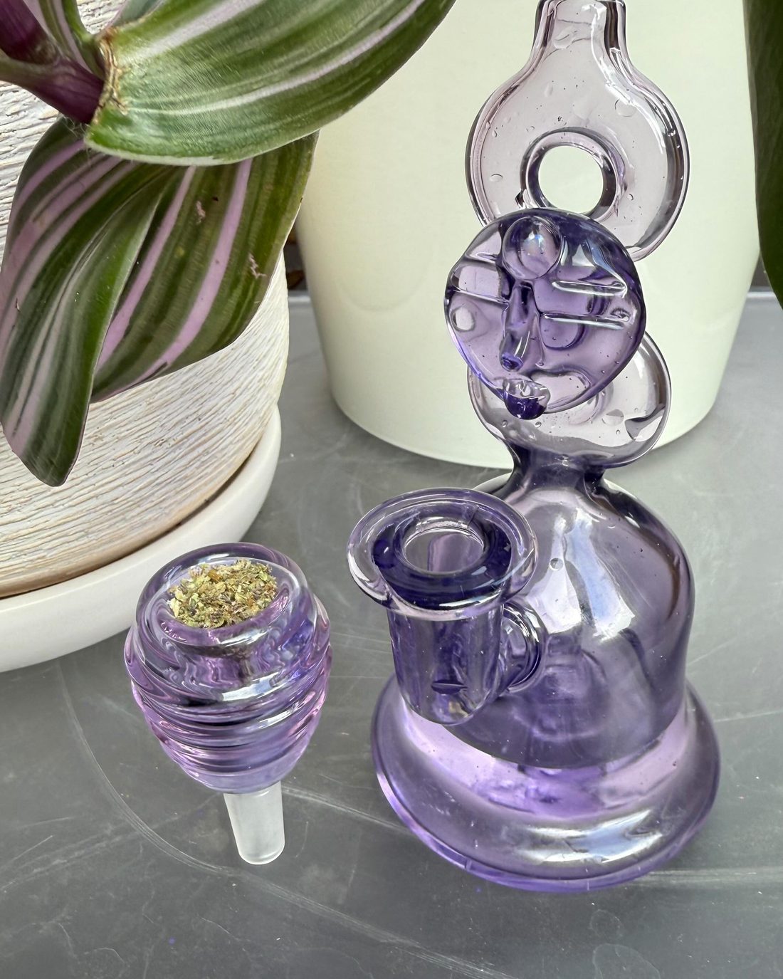 A hand-blown purple glass rig and matching bowl resting on a sunlit windowsill — part of the Purple Co. glass lineup